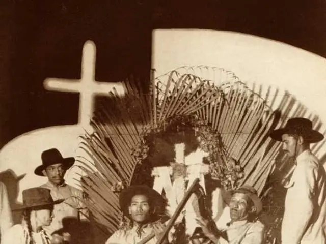 The image shows an old black and white photo of a group of people sitting on chairs in front of a...