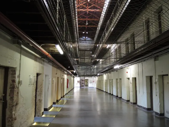 The image shows a long hallway in an old jail with a metal fence at the top, doors on the left and...