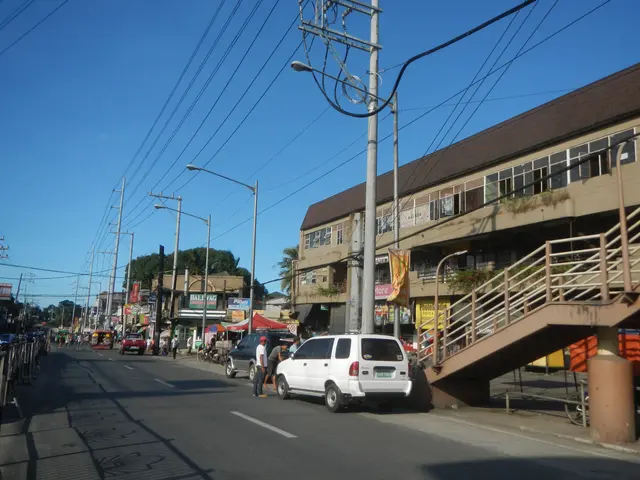 The image shows a city street with cars and people walking down it, electric poles with wires,...