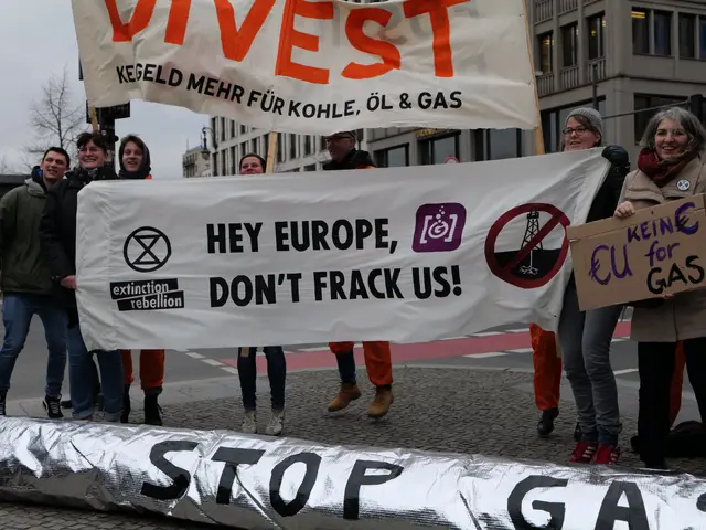 The image shows a group of people standing on the road, holding a banner that reads "Stop Gas" in...