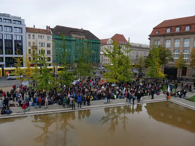 The image shows a large group of people standing around a pond in the middle of a city, surrounded...
