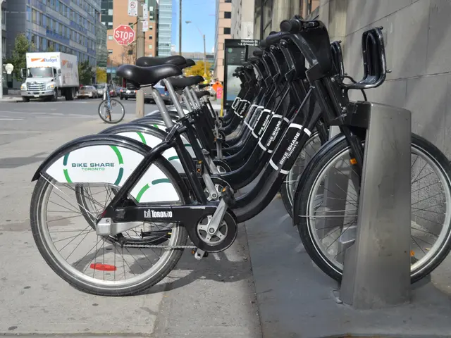 The image shows a row of bicycles parked on the side of a street, with a wall on the right side of...