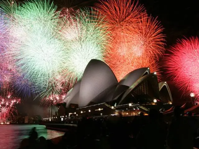 The image shows the Sydney Opera House illuminated by colorful fireworks during New Year's Eve...