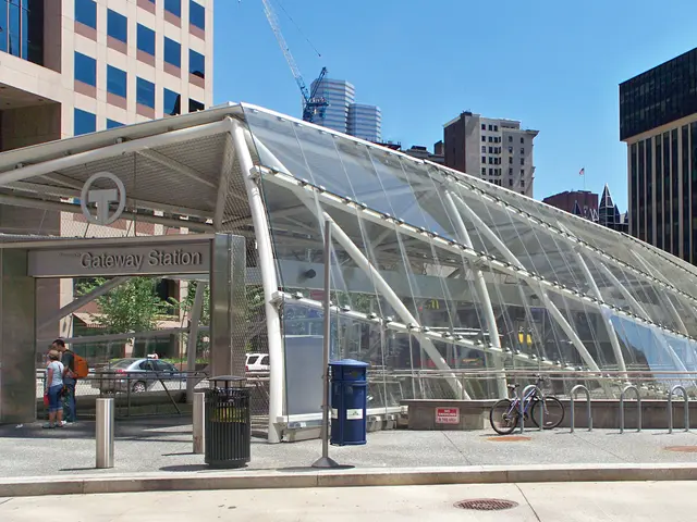 The image shows a bustling city street with tall skyscrapers, a bus stop with a glass roof, a group...