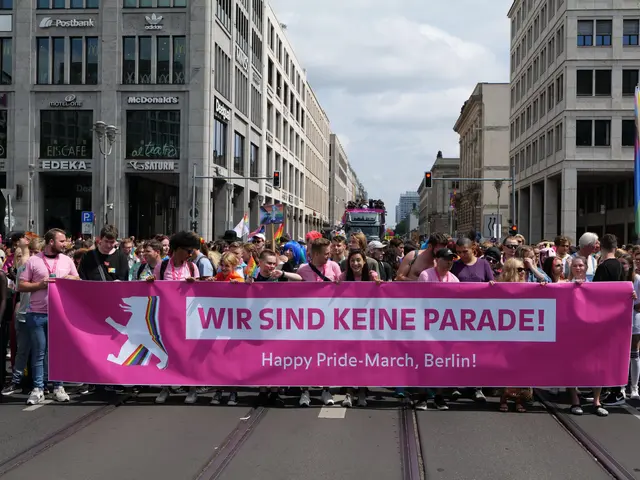 The image shows a group of people walking down a street in Berlin, Germany, holding a pink banner...