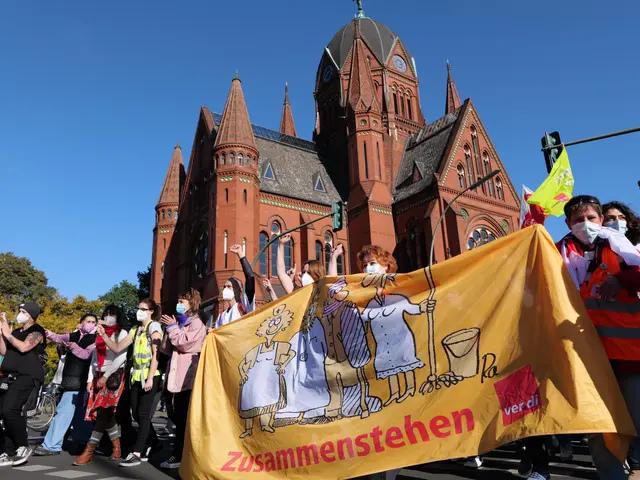 The image shows a group of people wearing masks and holding a yellow banner in front of a building...