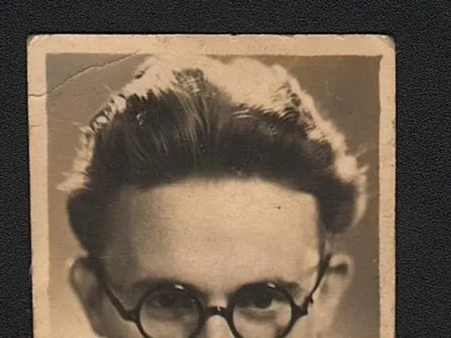 The image shows an old black and white photo of a man wearing glasses, with a black background and...