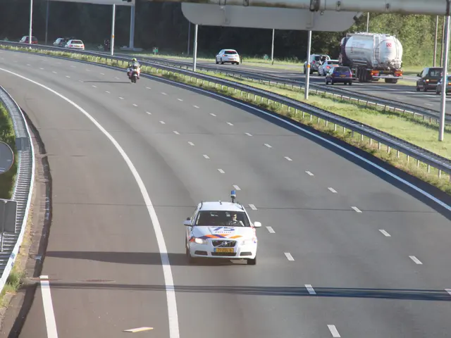 The image shows a car driving down a highway with a police car on the side of it. There are other...