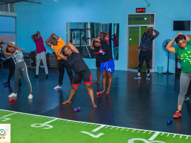 The image shows a group of people doing yoga in a gym. We can see them standing on the floor with...