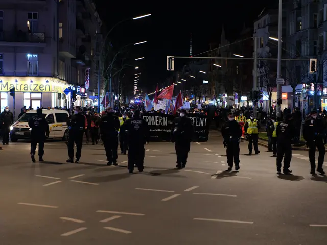 The image shows a group of people walking down a street at night, illuminated by street lights and...