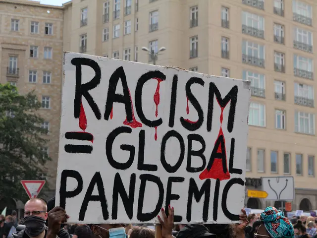 The image shows a group of people standing in front of a building, holding a sign that reads...