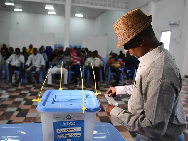 The image shows a man in a hat casting his vote at a polling station in Nairobi, Kenya. He is...