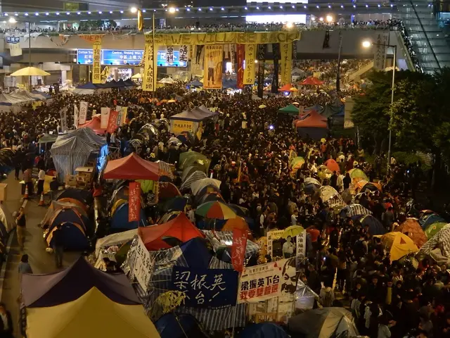 The image shows a large crowd of people standing around tents in the middle of a street. There are...