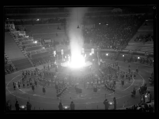 The image shows a black and white photo of a crowd of people in a stadium, illuminated by lights...