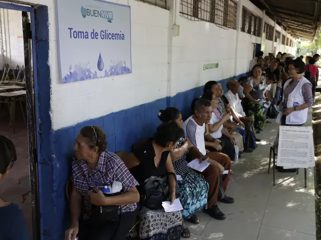 The image shows a group of people sitting on benches in front of a building, with a board on the...