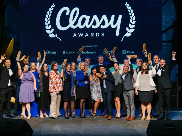The image shows a group of people standing on top of a stage, smiling and holding awards in their...