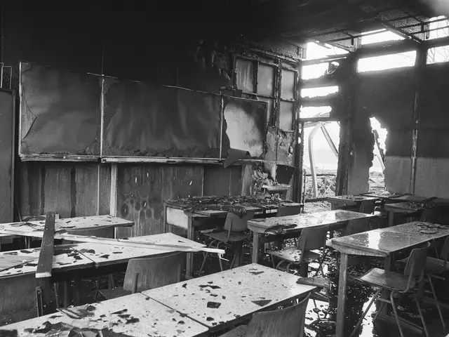 The image shows a black and white photo of a classroom with tables and chairs in it. The walls are...