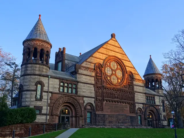 The image shows a large stone building with a clock tower on top of it, surrounded by windows,...