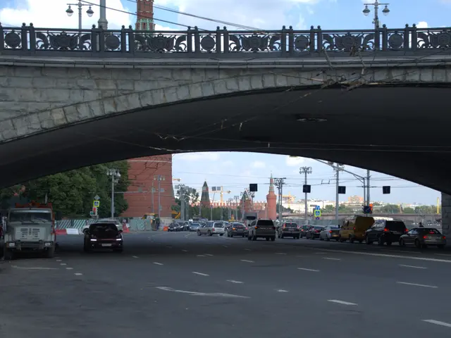 The image shows a bridge over a busy street with cars and trucks driving under it. On the left side...