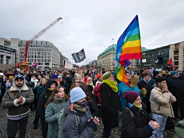 The image shows a large group of people standing in front of a building, holding flags and banners...