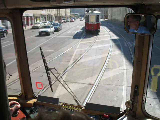 The image shows a man driving a tram on a city street, surrounded by other vehicles on the road. In...