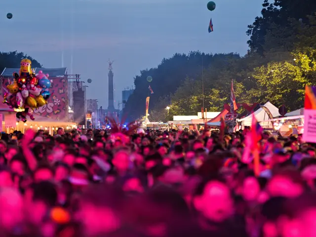The image shows a large crowd of people at a music festival at night, illuminated by colorful...