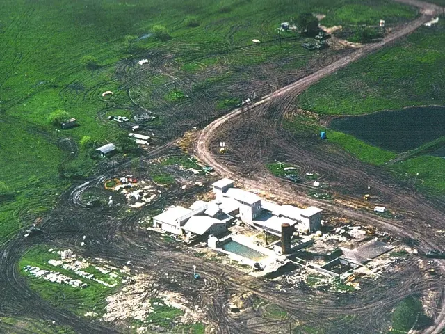 The image shows an aerial view of a farm in the middle of a field, surrounded by buildings, trees,...