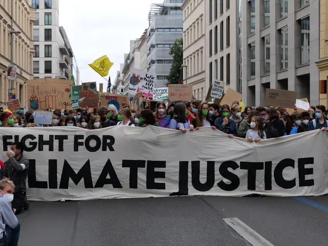 The image shows a group of people walking down a street, holding a banner that reads "Fight for...