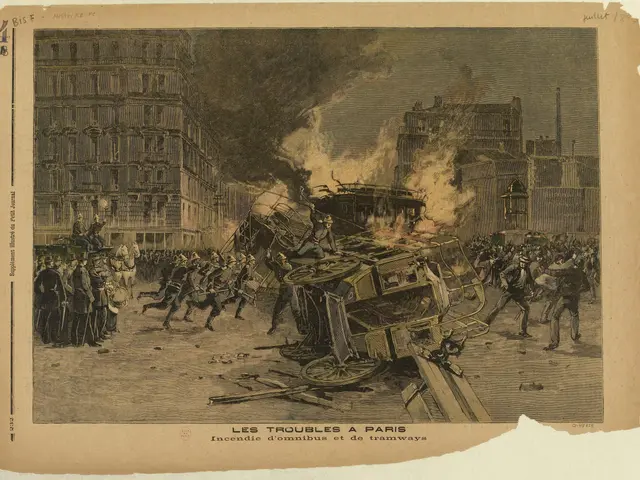 The image shows a group of people standing around a burning car in the middle of a street, with...