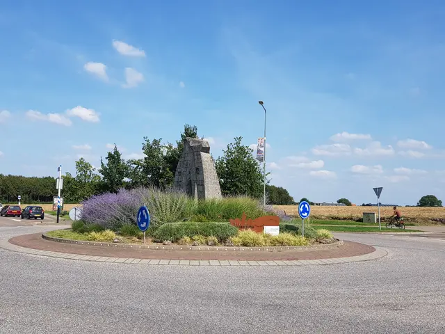 The image shows a roundabout in the middle of a parking lot with cars parked on the side of it....