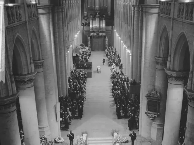 The image shows a black and white photo of a funeral procession in a church. There are many people...