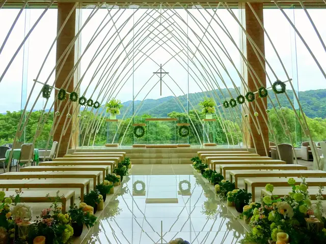 The image shows a wedding ceremony taking place inside of a large building with tables and chairs...