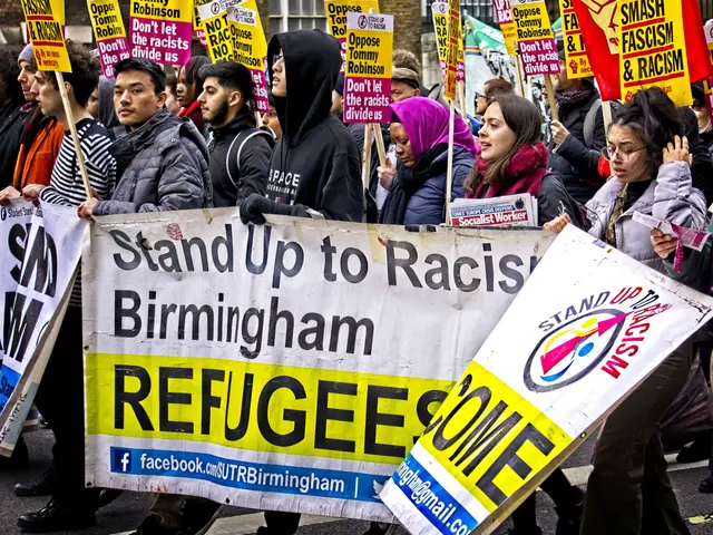 The image shows a group of people walking down a street, holding signs and banners with various...
