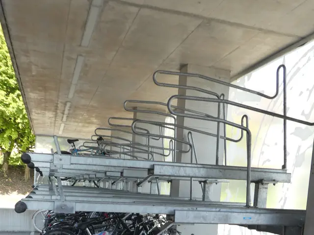 The image shows a bike rack with several bicycles parked on the side of a building. The wall on the...