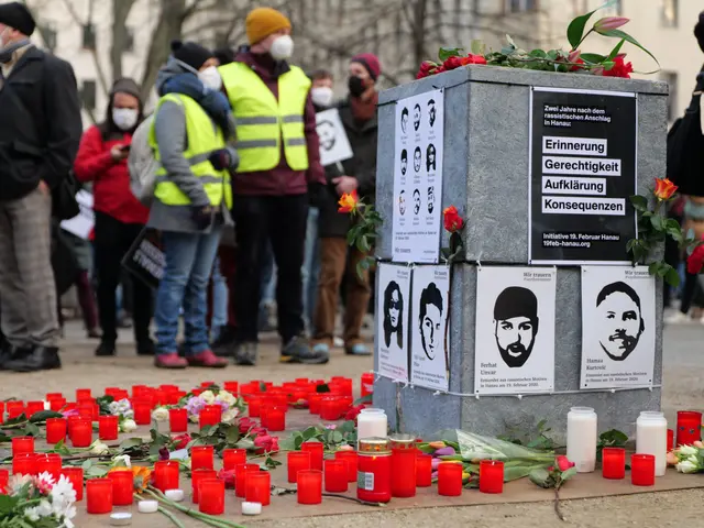 The image shows a group of people standing in front of a memorial with candles and flowers,...