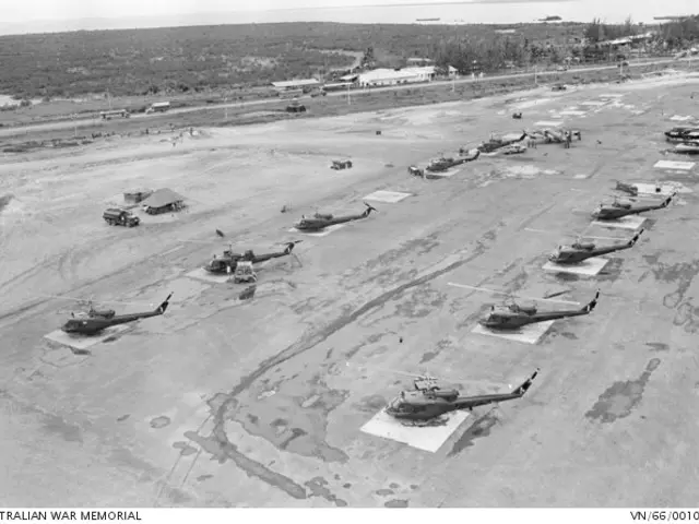 The image shows a black and white photo of several military helicopters parked on the ground...