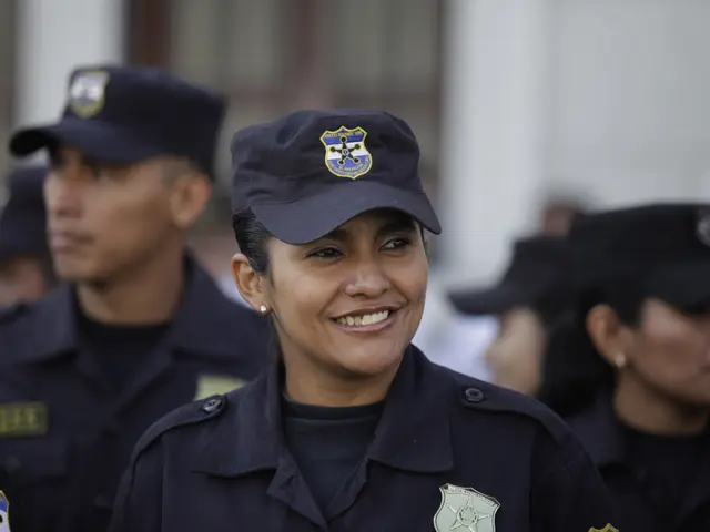 The image shows a woman in a police uniform standing in front of a group of people wearing caps and...