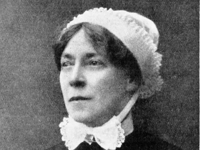 The image shows a black and white photo of a woman wearing a dress and a cap, with a badge on her...