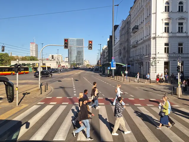 The image shows a group of people crossing the street at a crosswalk, with a bus on the left side...