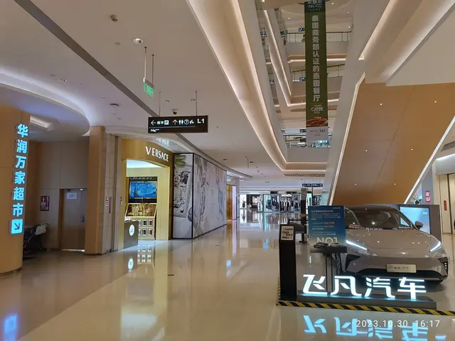 The image shows the interior of a shopping mall with a car parked in the middle of it. The floor is...