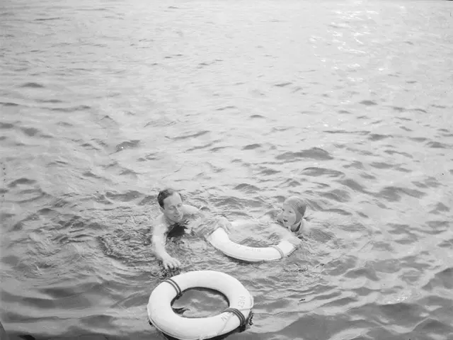 The image shows a man and a child swimming in the water with life preservers, surrounded by trees...
