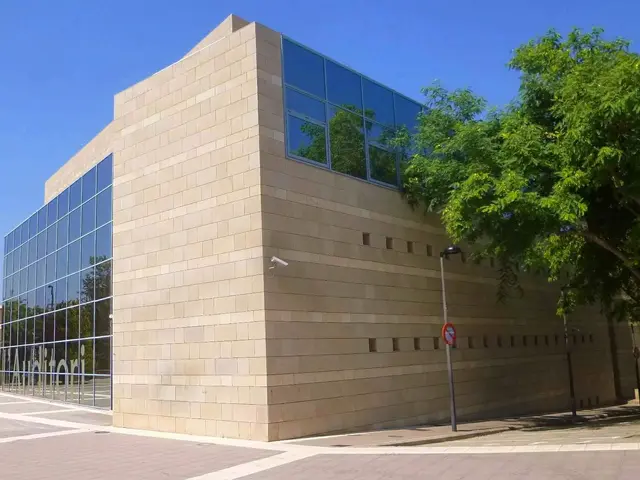 The image shows a large building with a lot of windows on the side of it, surrounded by street...