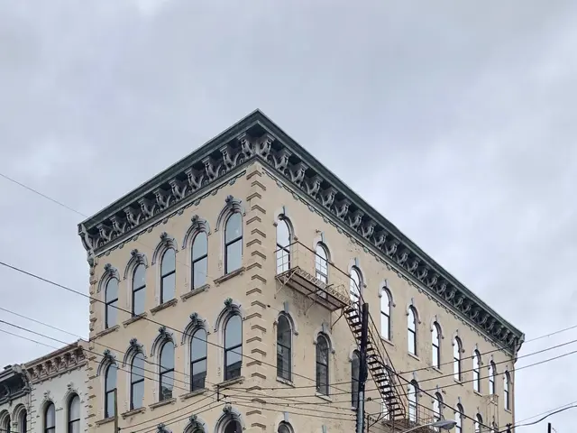 The image shows a large building on the corner of a street, with windows, a staircase, a signboard,...