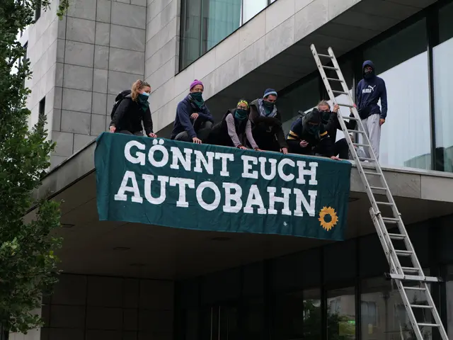 The image shows a group of people standing on top of a building, holding a banner with text on it....