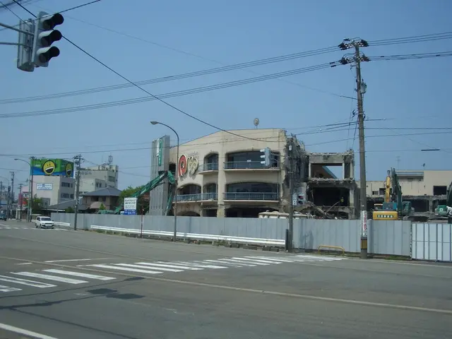 The image shows a city street with vehicles driving on it, electric poles with wires, light poles,...