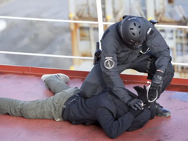 The image shows a man laying on the ground next to a police officer wearing a black dress, helmet,...