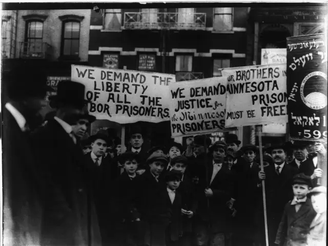 The image shows a group of people standing in front of a building, holding signs that read "We...