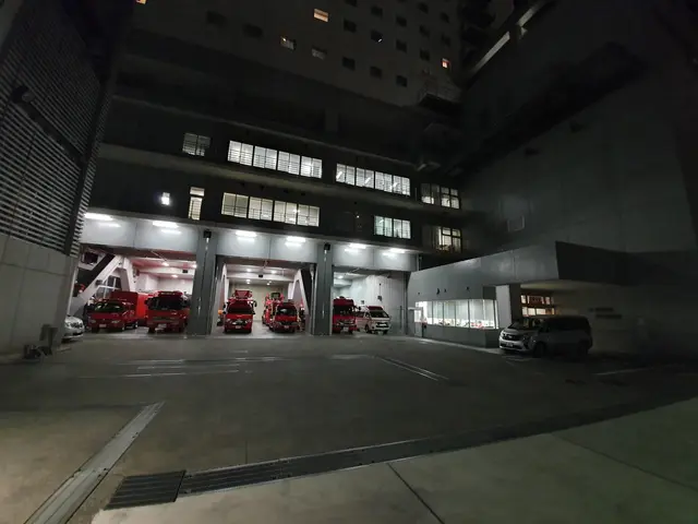 The image shows a parking garage at night with several fire trucks parked in it. The building has...