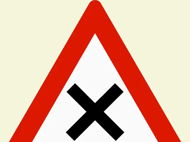 The image shows a red and white triangular road sign with a black cross on it, indicating that it...