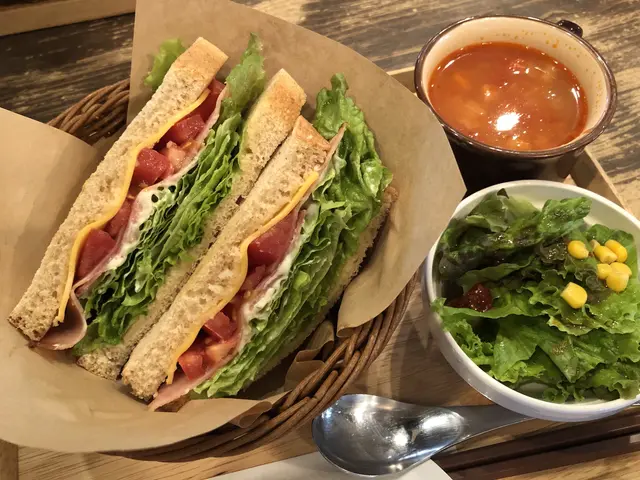 The image shows a wooden table with a basket containing a sandwich and a bowl of salad, as well as...